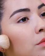 Close-up picture of a person applying bronzer to their cheek with a makeup brush